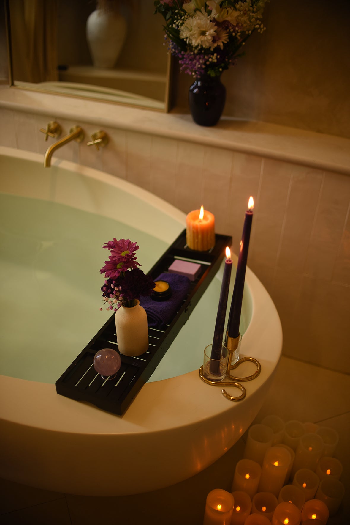 Bathroom scene with a bathtub, candles, and flowers.