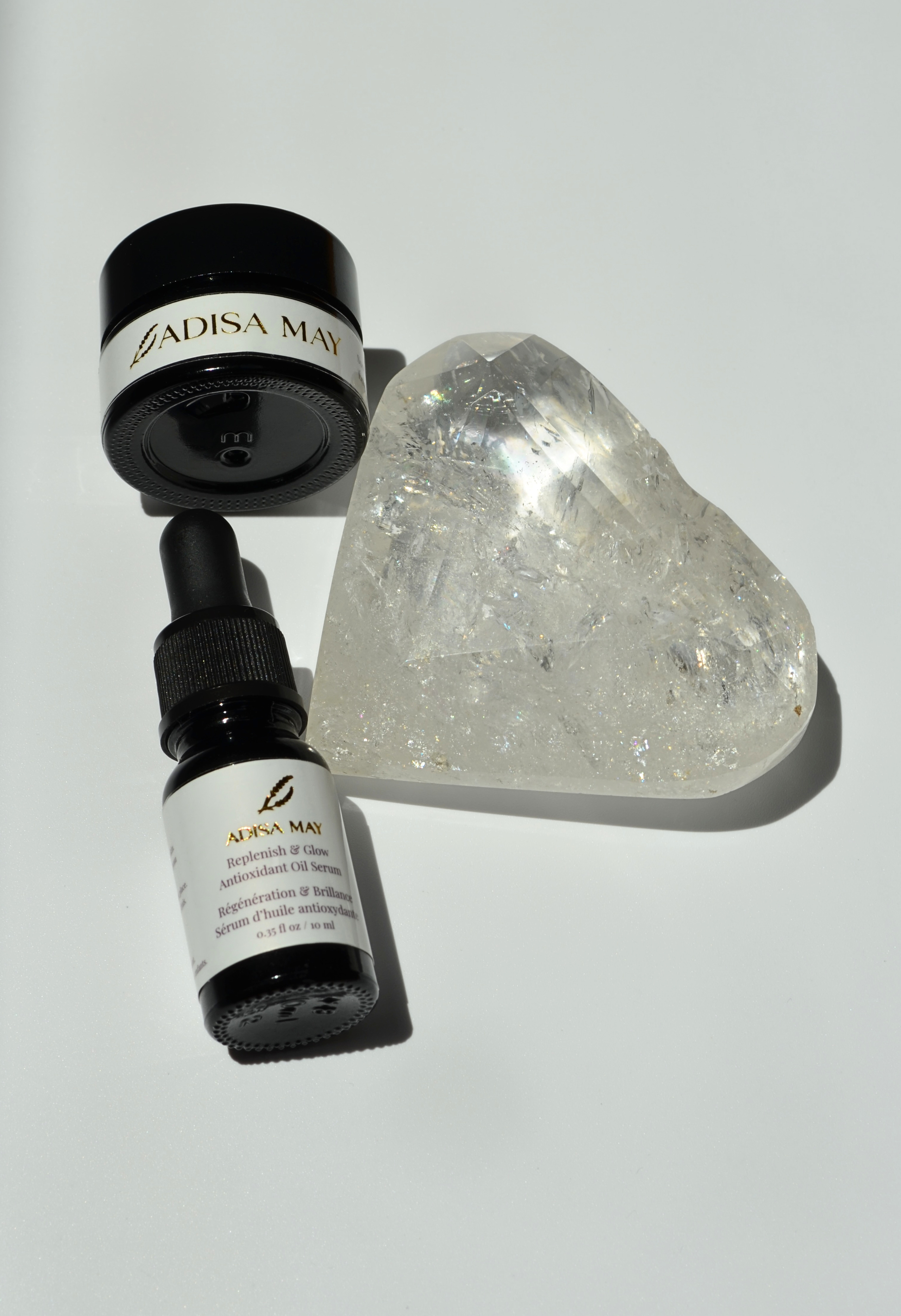 Two black bottles with white labels and a clear crystal heart on a light gray background