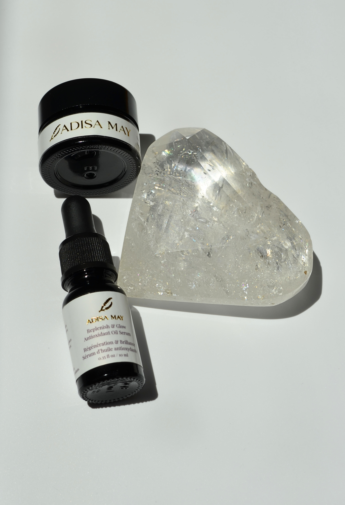 Two black bottles with white labels and a clear crystal heart on a light gray background