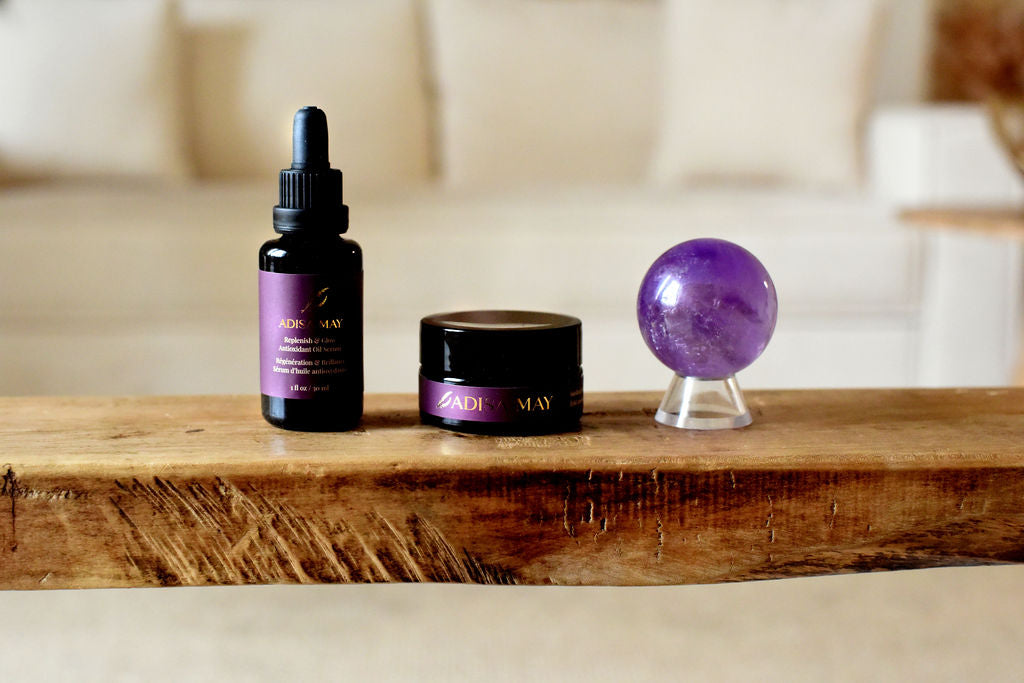 A black bottle and jar beside an amethyst sphere on a wooden bench