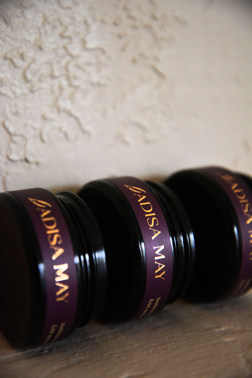 Three jars of Adisa May product on a textured surface