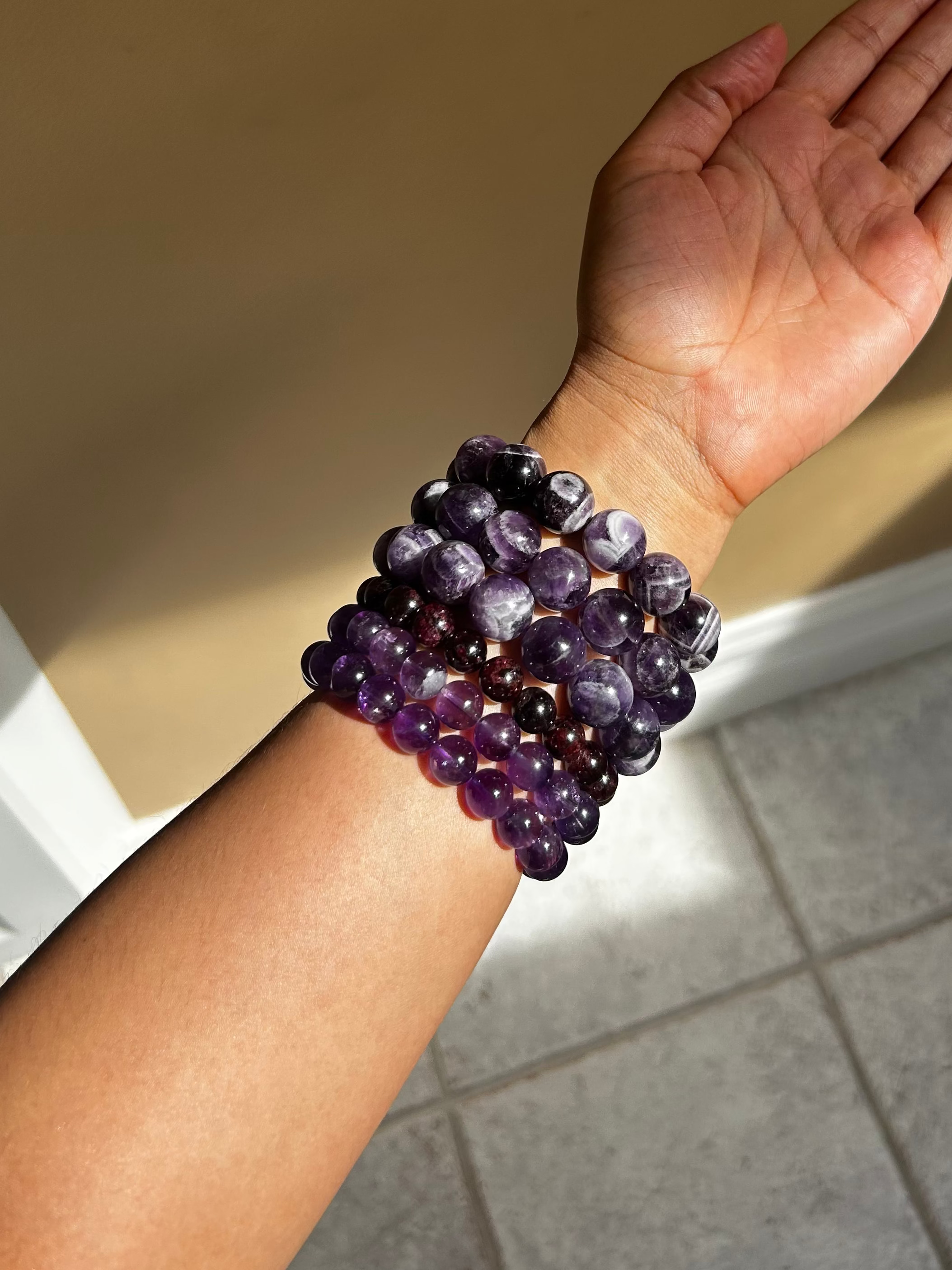 Hand wearing a purple beaded bracelet against a neutral background
