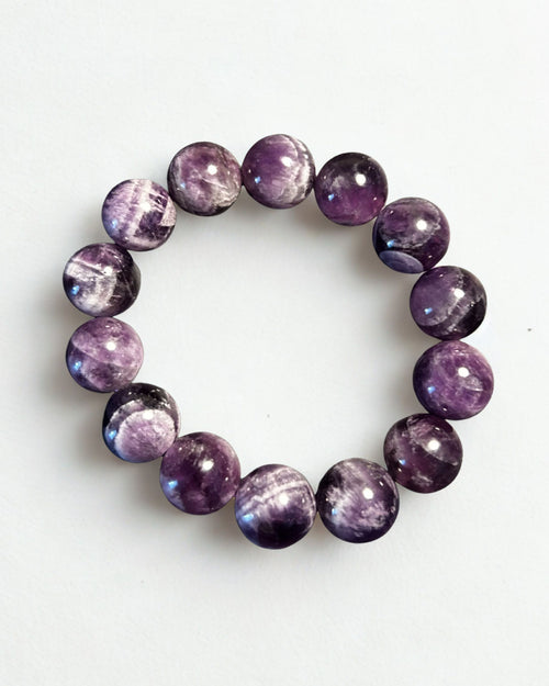 A beaded stretch bracelet made of polished round purple gemstone beads with natural white and dark marbling, displayed on a clean white background.