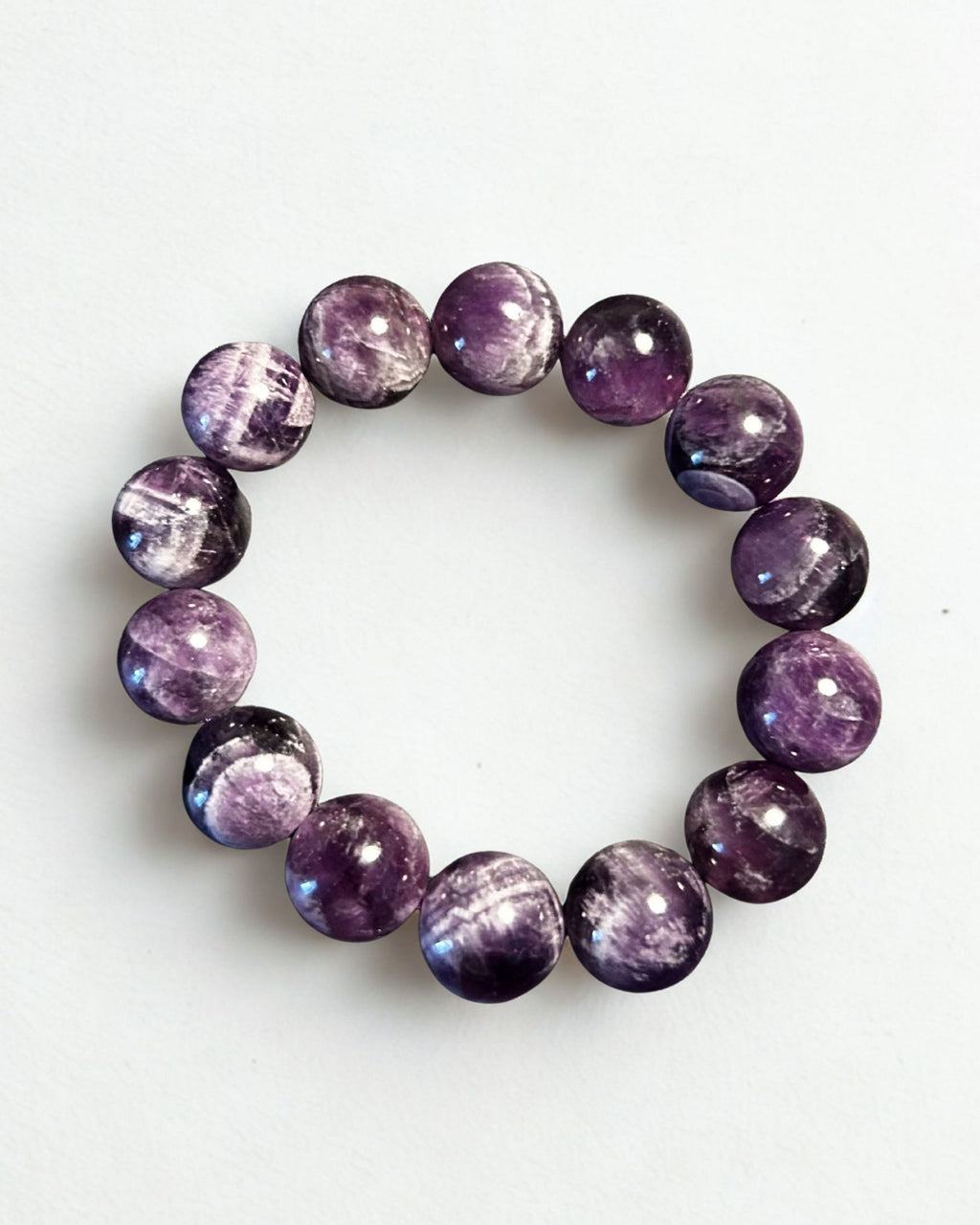 A beaded stretch bracelet made of polished round purple gemstone beads with natural white and gray crystalline patterns, displayed on a clean white background.