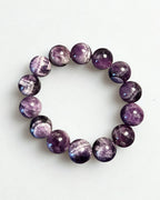 A beaded stretch bracelet made of polished round purple gemstone beads with natural white and gray crystalline patterns, displayed on a clean white background.