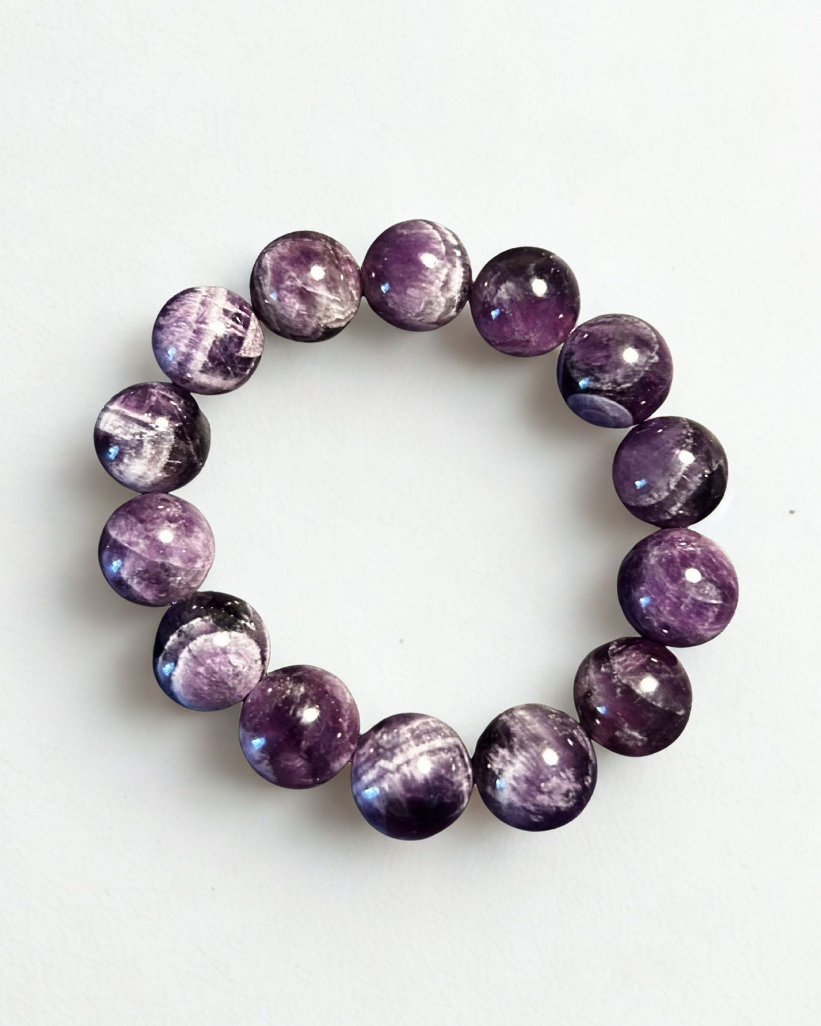 A beaded stretch bracelet made of polished round purple gemstone beads with natural white and gray crystalline patterns, displayed on a clean white background.
