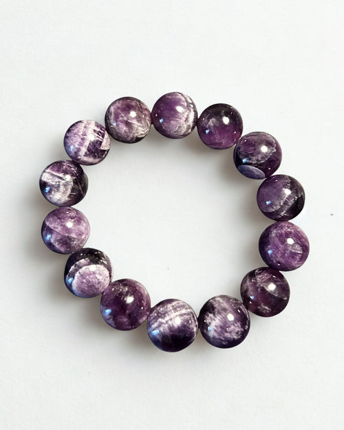 A beaded stretch bracelet made of polished round purple gemstone beads with natural white and gray crystalline patterns, displayed on a clean white background.