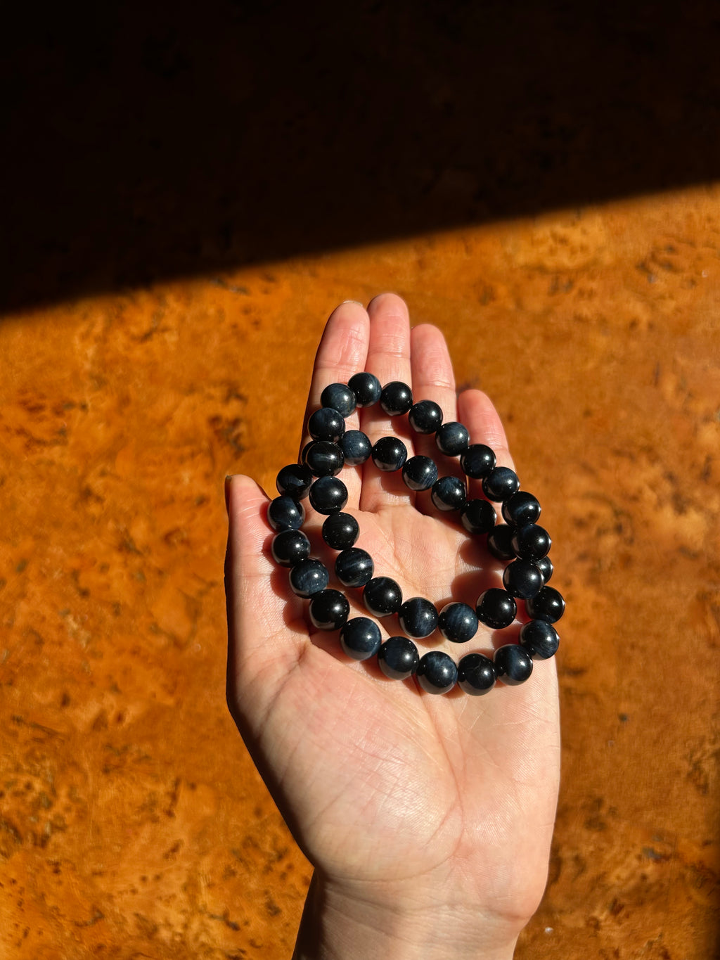 Hand holding two blue and black beaded bracelets on a wooden surface