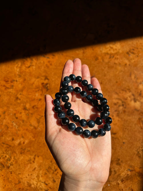 Hand holding two blue and black beaded bracelets on a wooden surface