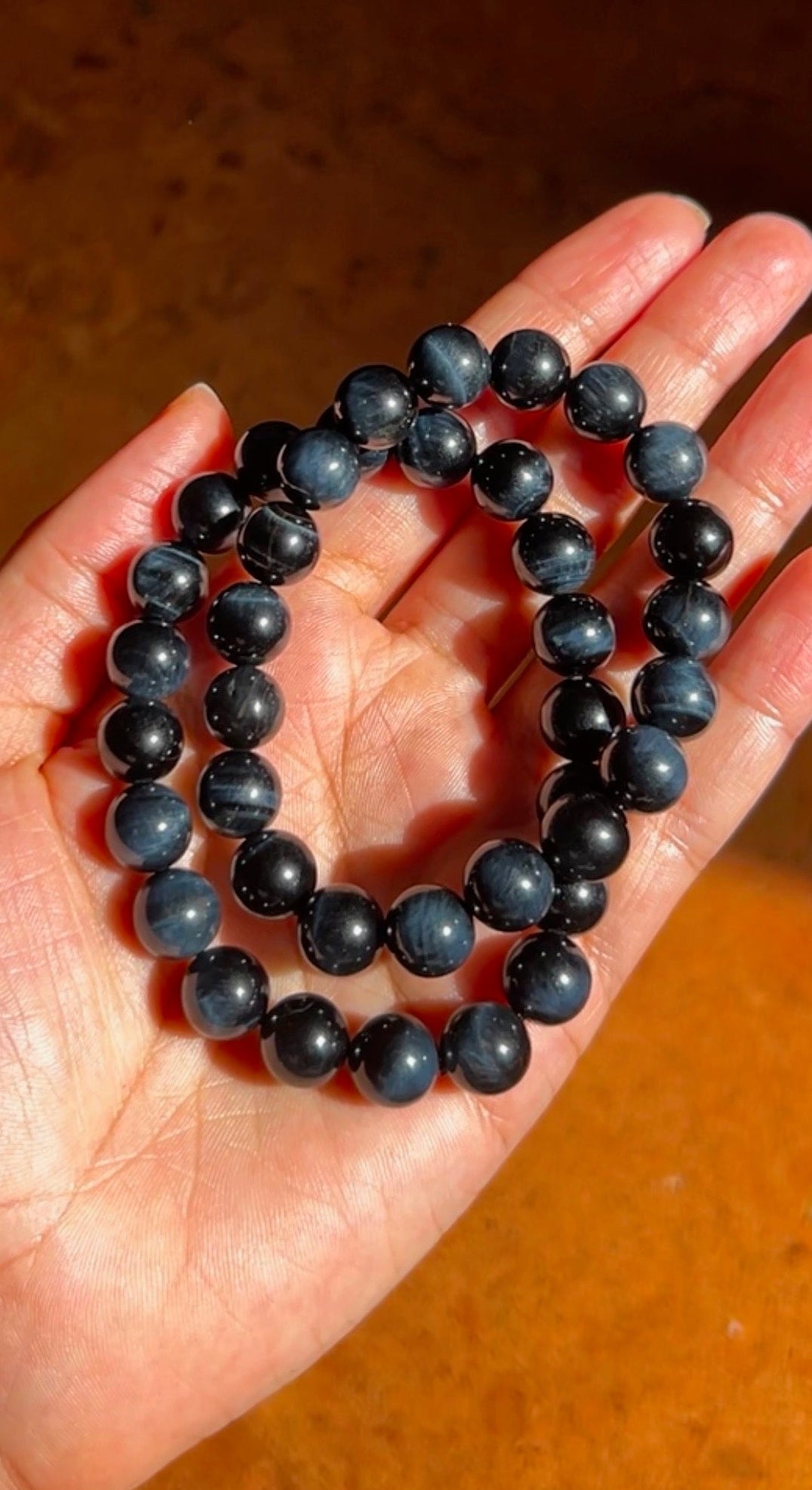 Hand holding two blue and black beaded bracelets on a wooden surface
