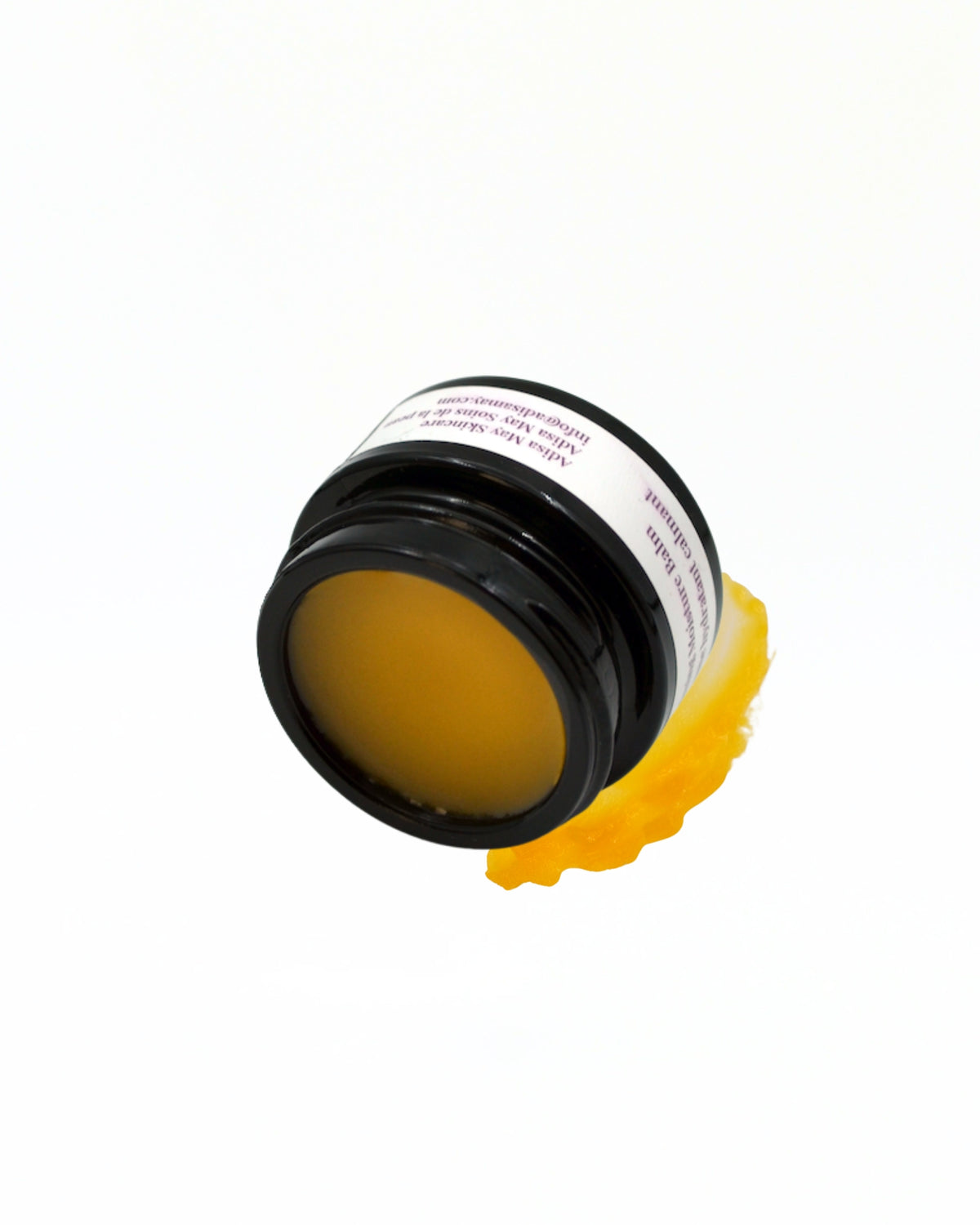 A small black jar of yellow balm or wax, tipped on its side with some of the yellow substance spilled underneath, on a plain white background.