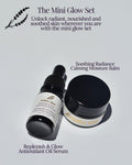 The Mini Glow Set by Africa May, featuring a black dropper bottle of Replenish & Glow Antioxidant Oil Serum and a black jar of Soothing Radiance Calming Moisture Balm on a light gray background with descriptive text.