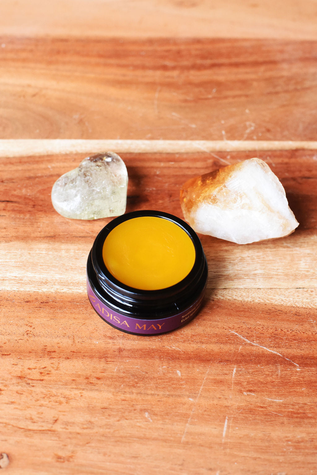 Jar of yellow moisturizer for dry and mature skin with a purple label on a wooden surface with crystals.