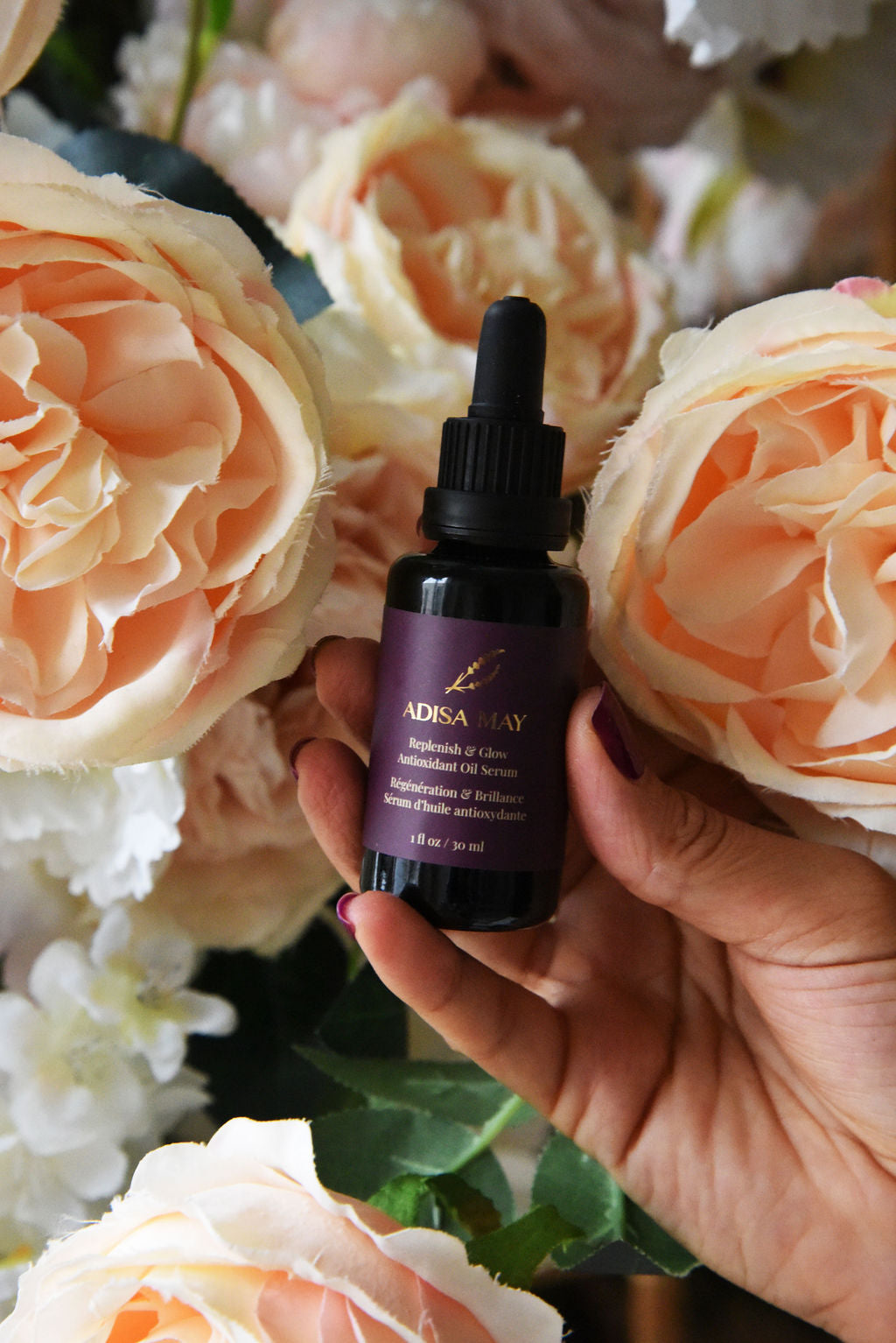 Hand holding a bottle of Adisa May skincare product with flowers in the background