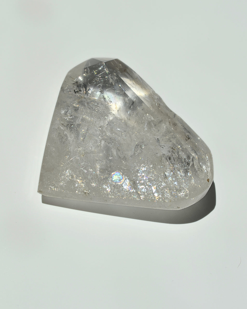 A raw, unpolished clear quartz crystal point with natural inclusions, displayed on a clean white background with a soft shadow.