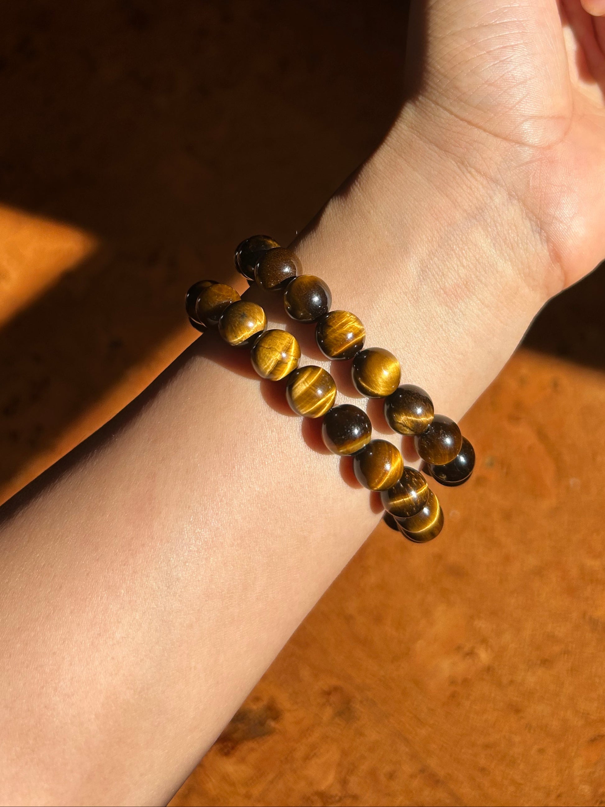 Hand wearing a tiger eye bracelet on a wooden surface
