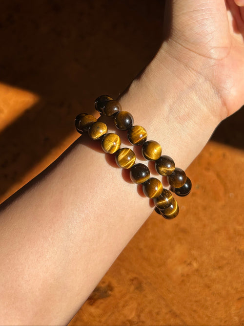 Hand wearing a tiger eye bracelet on a wooden surface