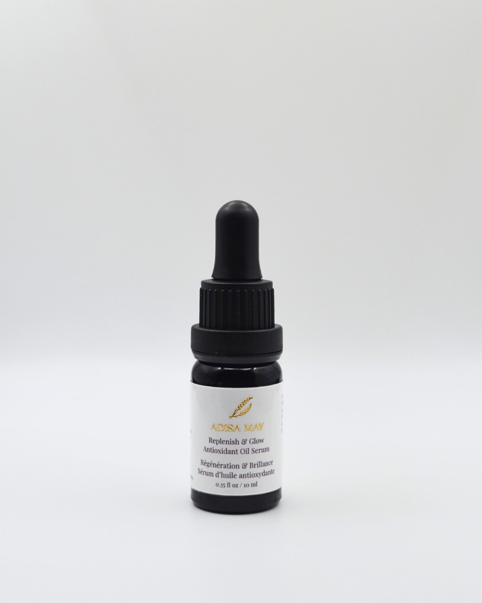 A small dark glass dropper bottle with a black cap and a white label, centered on a light gray background. The label reads 'ADISA MAY' and 'Replenish & Glow Antioxidant Oil Serum'.