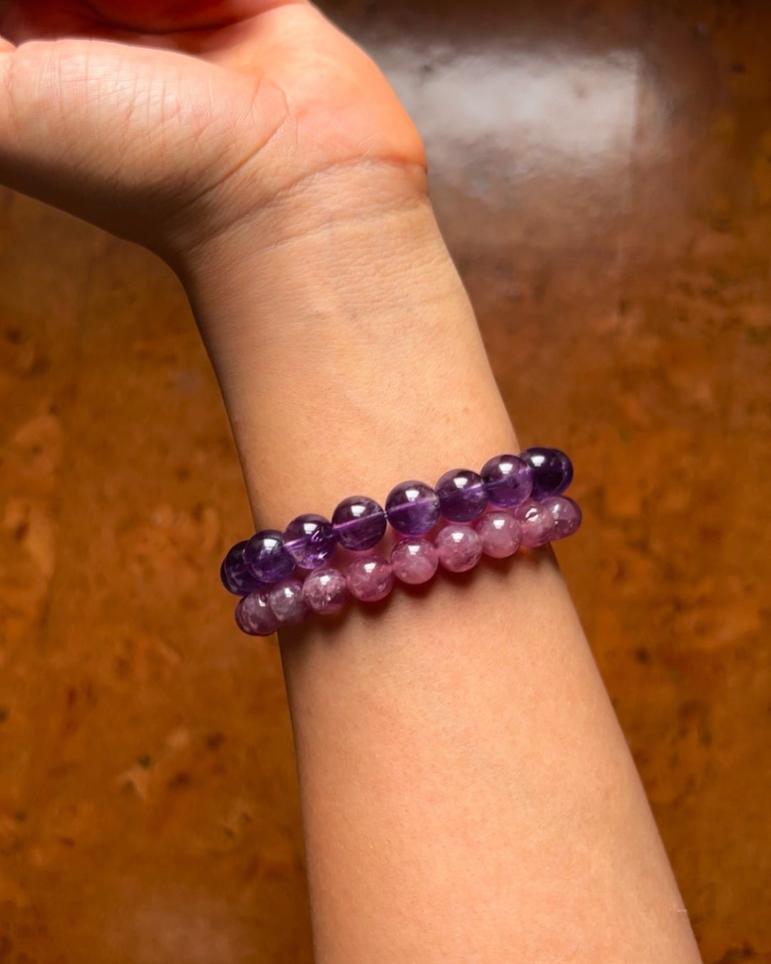 Two beaded bracelets, one purple and one pink, on a wrist against a wooden background.