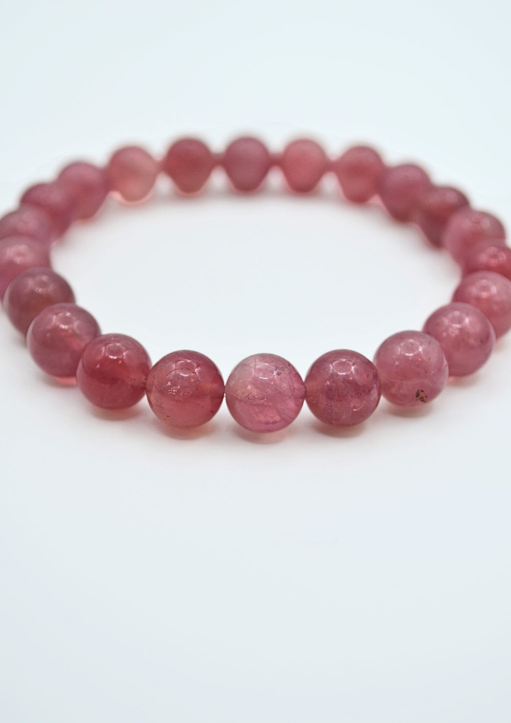 A beaded stretch bracelet made of faceted, translucent pinkish-red round beads, photographed on a clean white background.