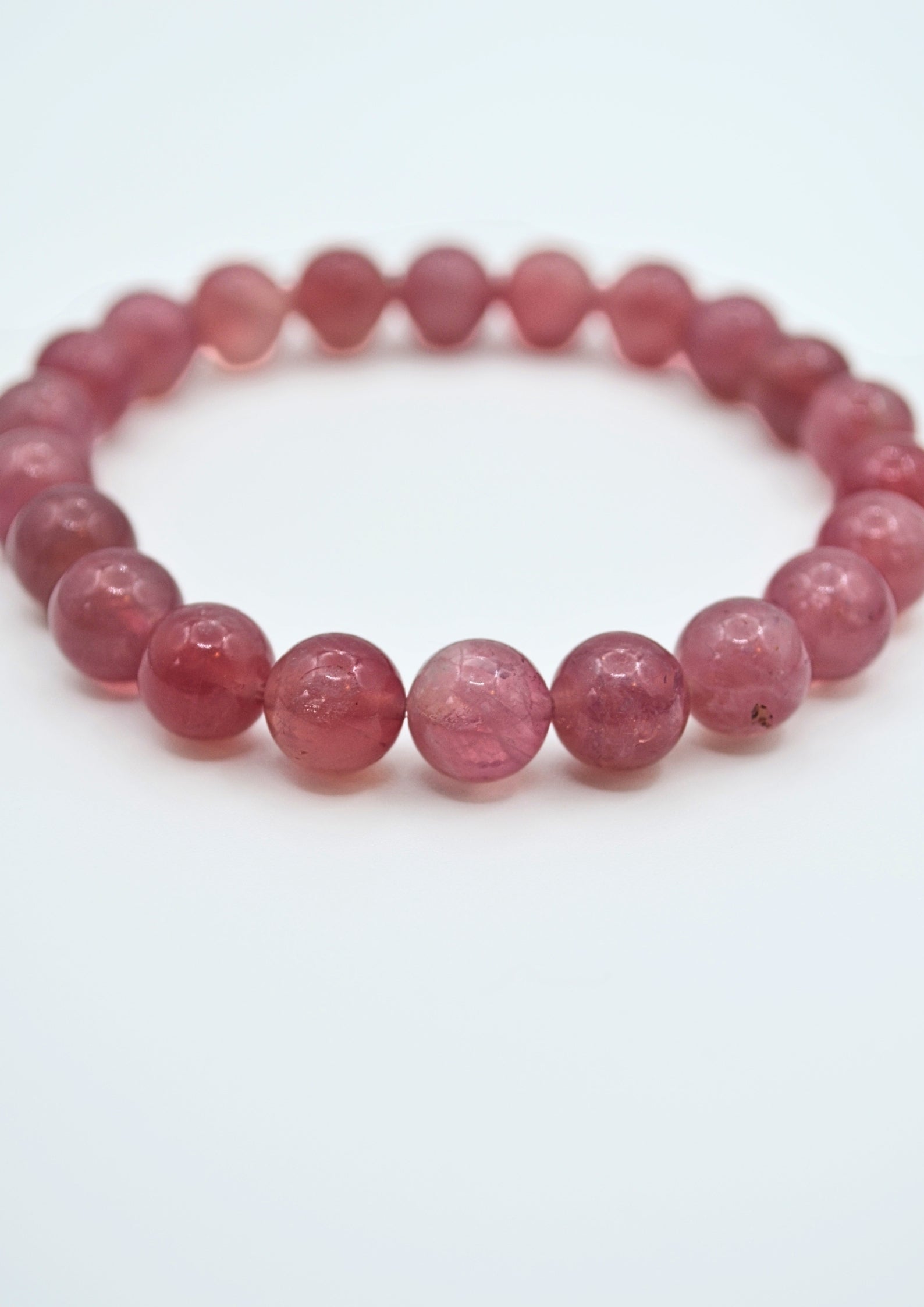 A beaded stretch bracelet made of faceted, translucent pinkish-red round beads, photographed on a clean white background.