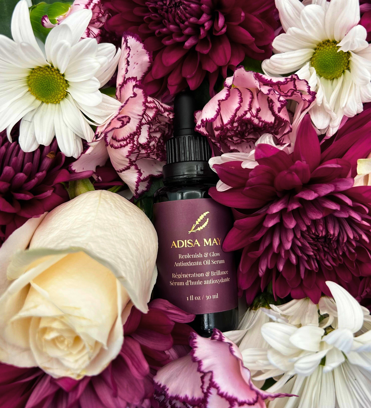 Adisa May serum bottle surrounded by a bouquet of white and purple flowers