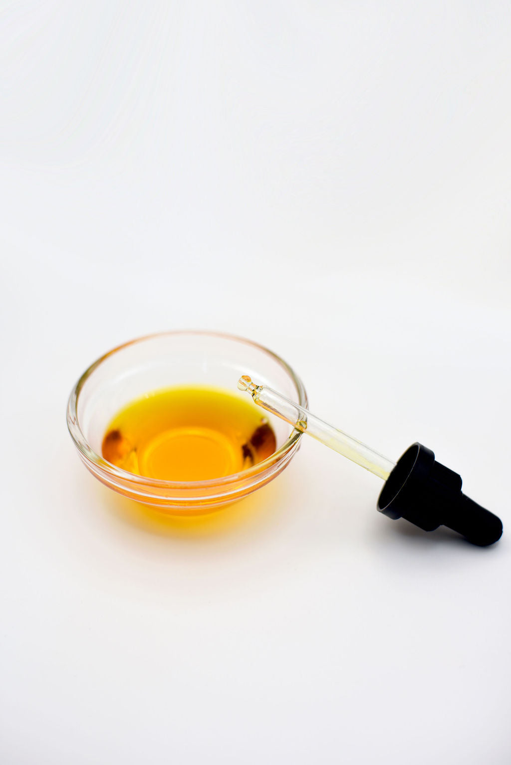 Glass bowl with yellow liquid and dropper on a white background