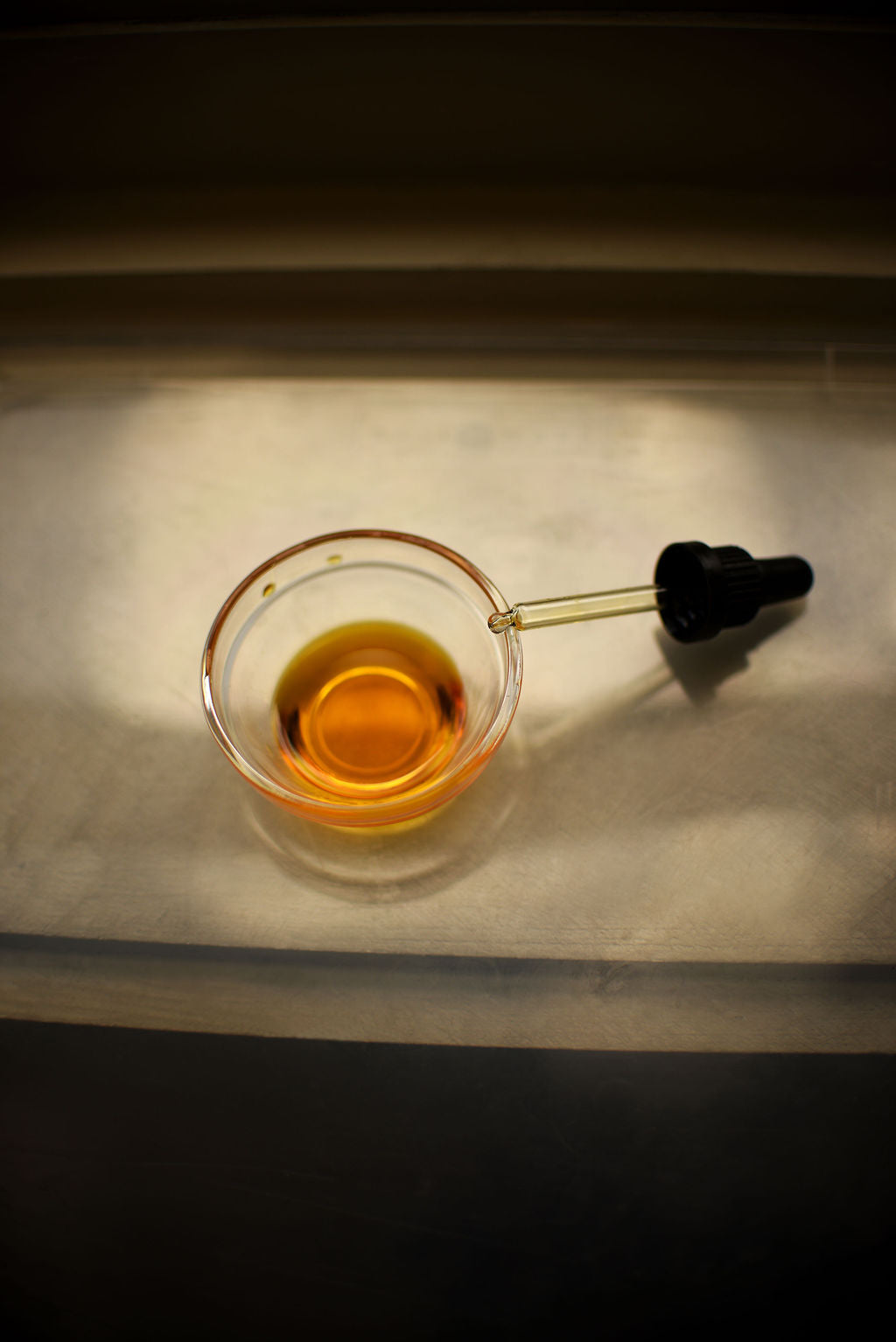 Glass container with amber liquid and dropper on a reflective surface