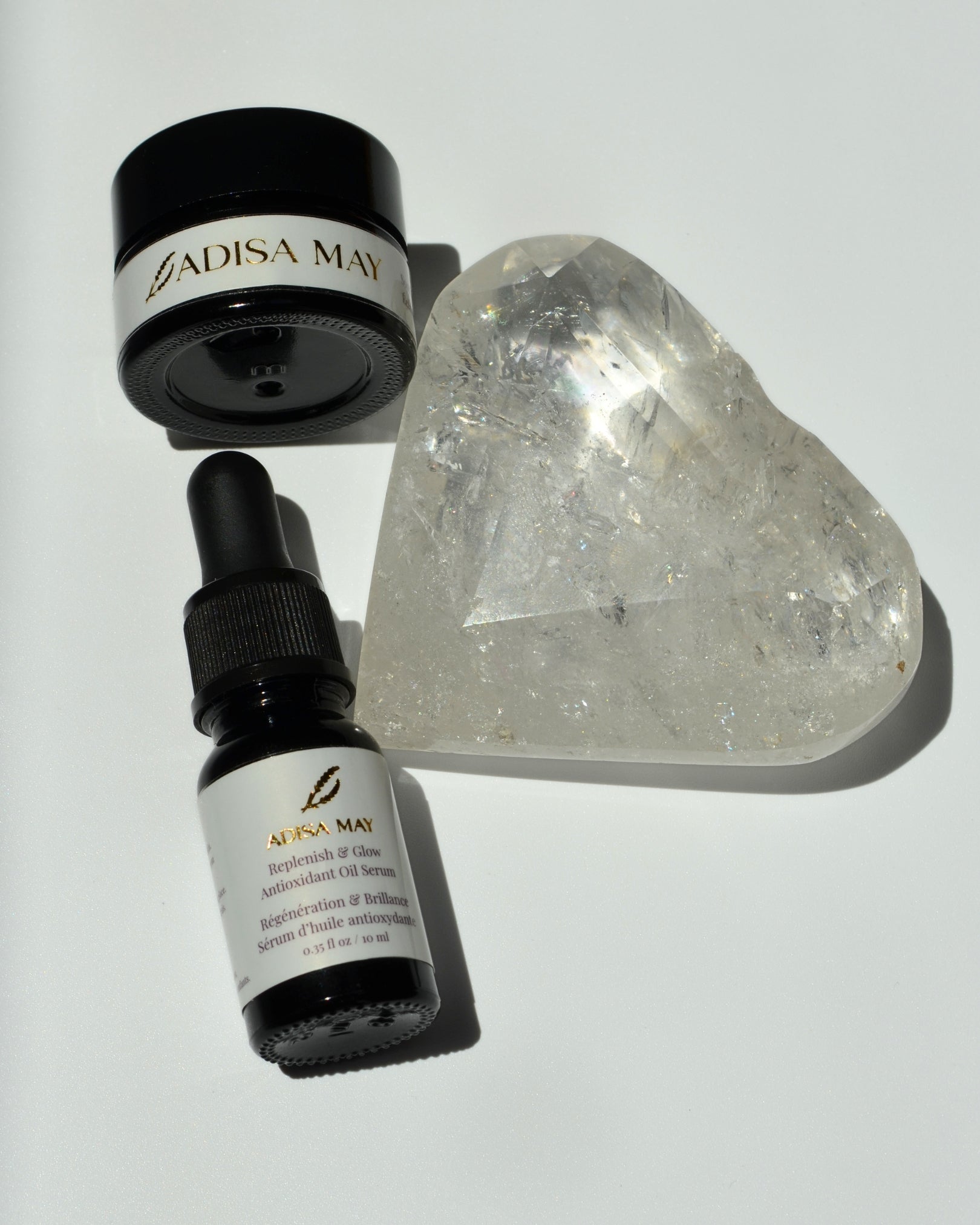 One bottle one jar with white label on it on a white background with a clear quartz crystal shaped as a heart beside them 