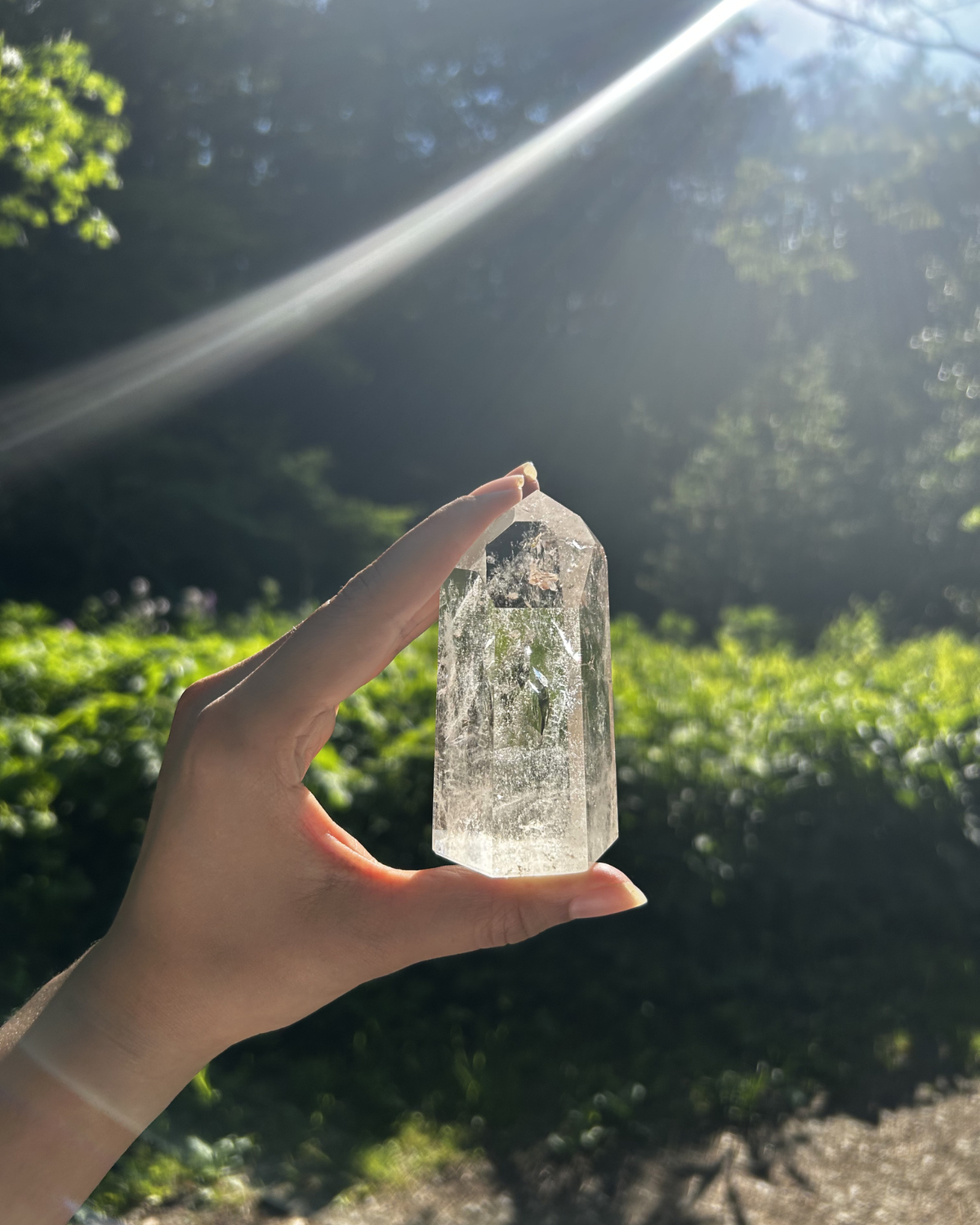 Hand holding a clear crystal against a natural background with sunlight