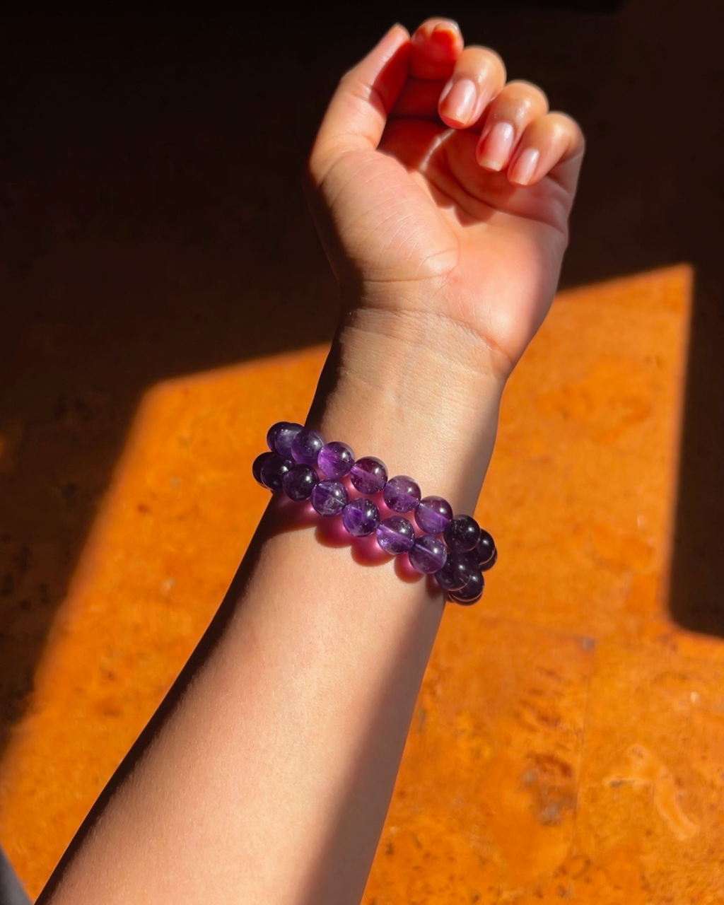 Hand wearing a purple beaded bracelet on an orange surface