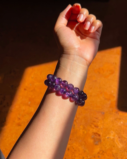 Hand wearing a purple beaded bracelet on an orange surface
