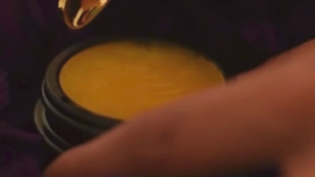 An orange cream in a black jar with a golden spoon on a dark purple background