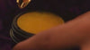 An orange cream in a black jar with a golden spoon on a dark purple background